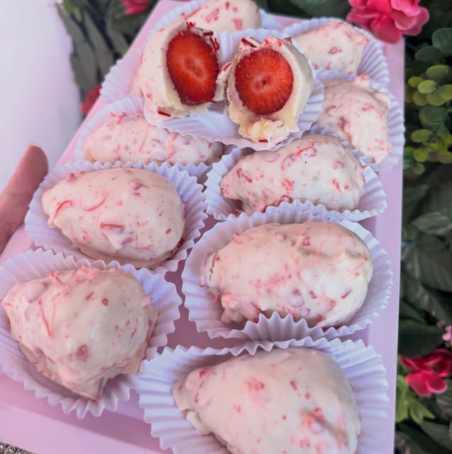 Bombons de morango cobertos com chocolate branco, um deles cortado ao meio